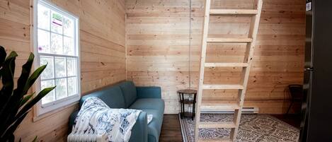 L’intérieur d’une cabane en bois, avec un canapé bleu, une échelle, un radiateur et un réfrigérateur.