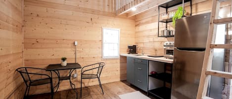A compact kitchen with wooden walls, a dining area with a table and chairs, and a refrigerator.