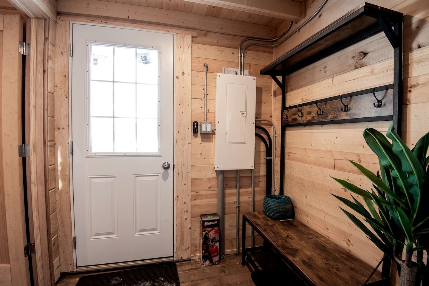 Ein Holzkamin mit einer weißen Tür, einer Bank, einem Regal mit Haken und einer grünen Pflanze.