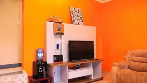 Una sala de estar con televisor de pantalla plana sobre un mueble de madera, un sofá y un dispensador de agua.
