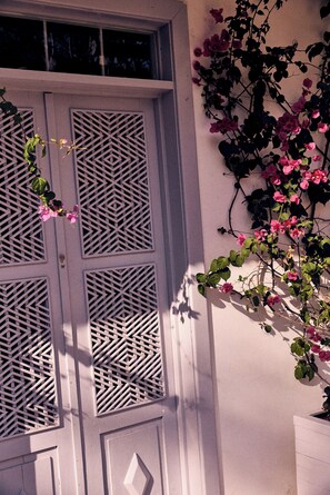 Eine Gebäudefassade mit einem geometrischen Fensterdesign und einer Kletterpflanze mit rosa Blüten.