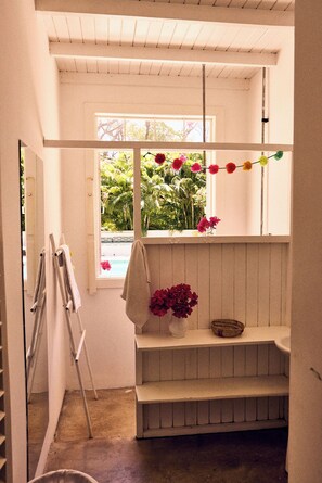 A room with a wooden bench, a window with a view of greenery, and a wall-mounted shelf with a basket. - Serene 4-bedroom house in Guanacaste, Costa Rica, perfect for relaxing getaway (Los Pargos)