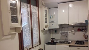 Uma cozinha compacta com armários brancos, forno embutido, cafeteira e uma pequena mesa.