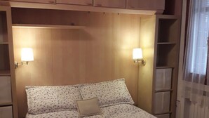 Uma cama com roupa de cama floral, duas luminárias fixadas na parede e um ventilador de teto.