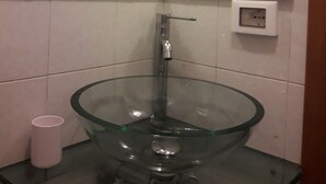 Uma casa de banho com uma pia de vidro, um espelho e uma janela com moldura de madeira.