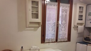 Uma cozinha pequena com uma cadeira de madeira, bancada branca e armário sobre a pia.
