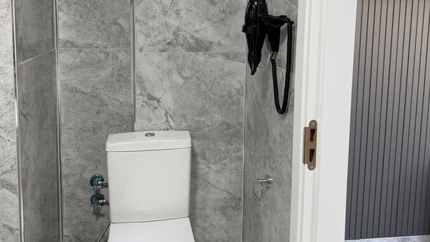 Baño con inodoro, ducha y secador de pelo fijado a la pared.