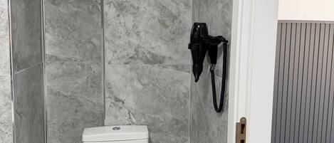 A bathroom with a toilet, a shower, and a hairdryer mounted on the wall.