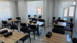 Un moderno salón de conferencias con varias mesas y sillas, ventanas amplias con cortinas translúcidas y luces en el techo.