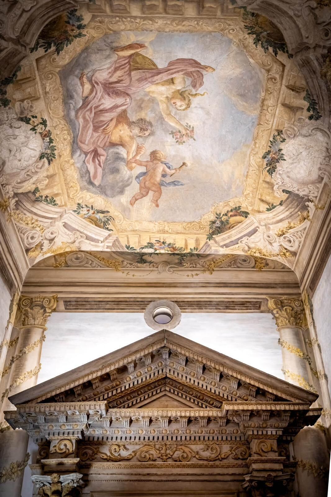 A classical architectural ceiling with a fresco, ornate columns, and a detailed pediment.