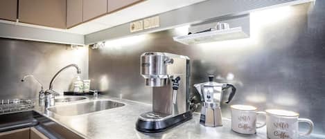 Una cocina moderna con electrodomésticos de acero inoxidable, incluyendo una cafetera y un hervidor, y dos tazas con detalles relacionados al café.