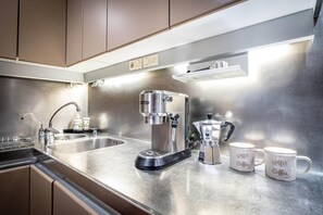 Eine moderne Küche mit Edelstahlgeräten, darunter eine Kaffeemaschine und ein Wasserkocher, sowie zwei Tassen mit Kaffee-Bezug.
