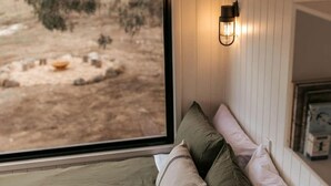 Une chambre comprenant un lit, des oreillers, une table de chevet, une fenêtre donnant sur un espace extérieur et un luminaire fixé au mur.