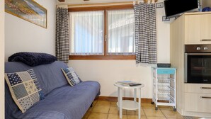 Una habitación acogedora con un sofá, una mesita, un televisor y una zona de cocina.