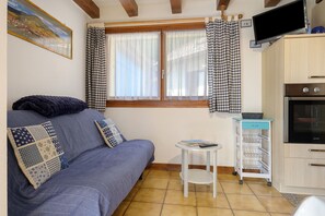 A cozy room with a sofa, a small table, a television, and a kitchen area. - Holiday Home 'Gite Muscat - Kaysersberg Vignoble' with Mountain View, Wi-Fi and Air Conditioning (Kaysersberg-Vignoble)