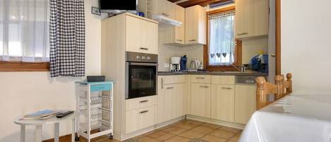 A compact kitchen with a built-in oven, a coffee maker, and a small table with a basket.