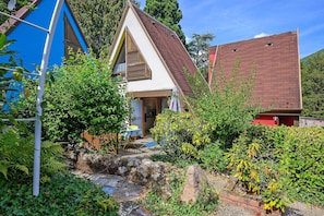 A house with a sloped roof, a visible front door, and a garden with various plants and a small stream. - Holiday Home 'Gite Muscat - Kaysersberg Vignoble' with Mountain View, Wi-Fi and Air Conditioning (Kaysersberg-Vignoble)