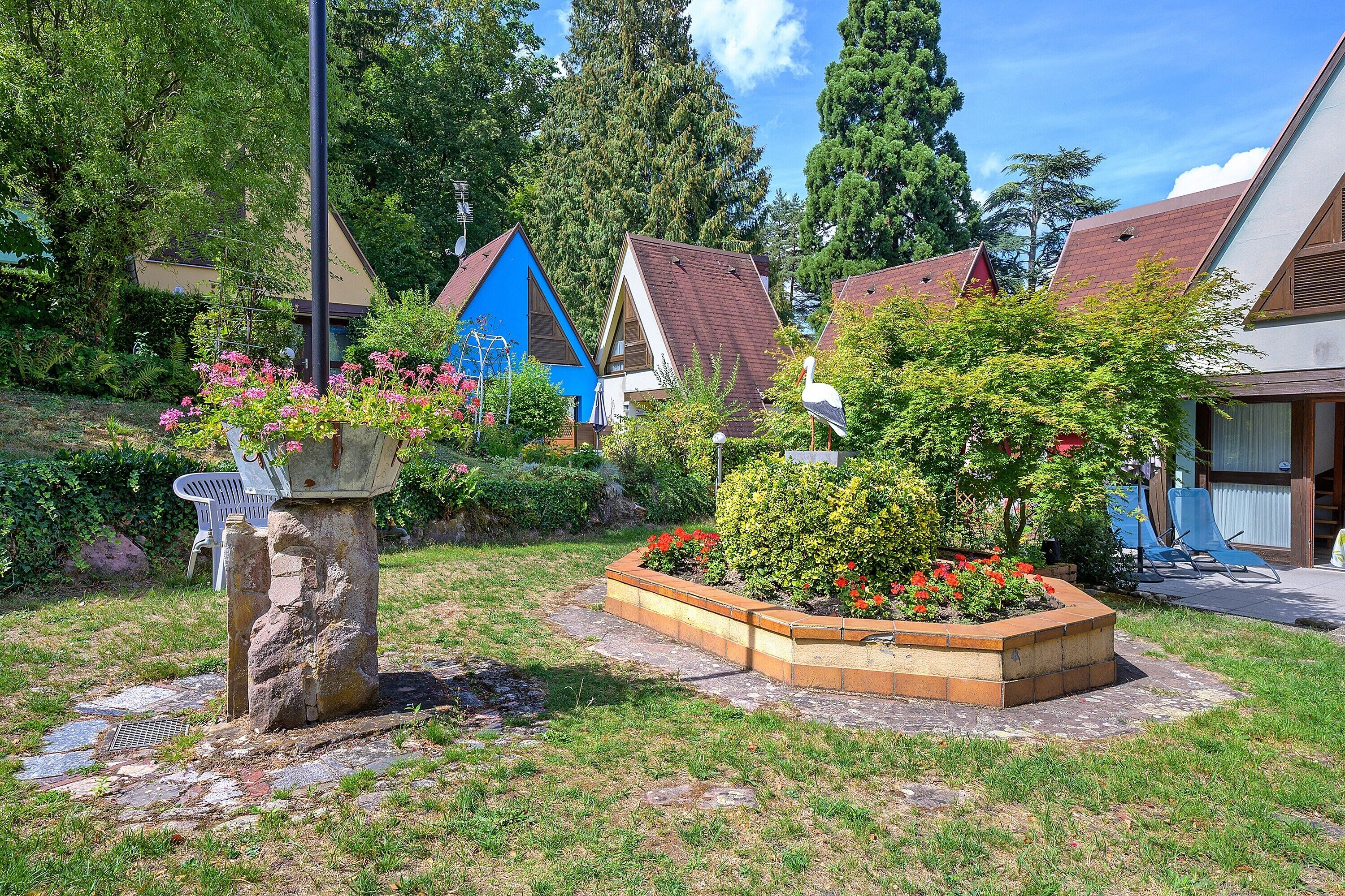 A garden with a stone bench, flower beds, and a blue house in the background.