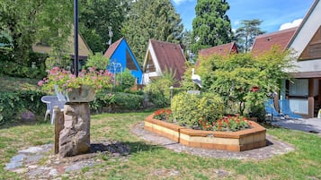 A garden with a stone bench, flower beds, and a blue house in the background.