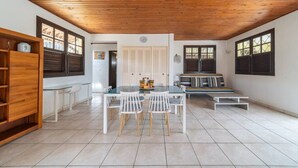 A spacious room with a wooden ceiling, a dining area with a table and chairs, a sofa, and a window with shutters. - Villa Zenaida, a villa near the sea (Sainte-Luce)