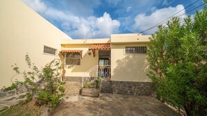 A two-story building with a stone-paved entrance, a tiled roof, and a small garden area with various plants. - Villa Zenaida, a villa near the sea (Sainte-Luce)