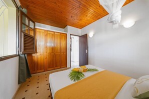 Quarto com cama, guarda-roupa de madeira, janela com persianas e teto com vigas de madeira.