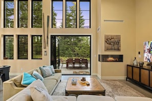 A spacious living room with a large window, a fireplace, and a dining area with outdoor seating. - 4BR, Hot Tub, Firepit, Fireplace, Pet Friendly (Cle Elum)
