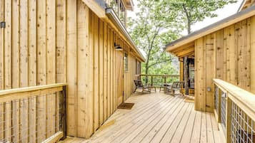 A wooden deck with a metal railing, a table and chairs, and a door leading to an interior space.