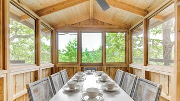 Un comedor con una mesa larga dispuesta para una comida, rodeado de paneles de madera y ventanas grandes.