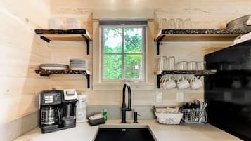 A compact kitchen with a window, shelves for dishes, a coffee maker, and a sink.