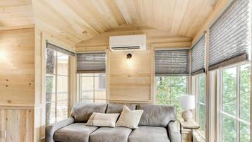 Un interior de madera con sofá, equipo de aire acondicionado y ventanas amplias.