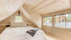 Un dormitorio con techo inclinado, cama con ropa de cama a cuadros y ventanas con vistas al exterior.