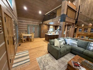A spacious living area with a wooden floor, a green sofa, a dining table with chairs, and a kitchen in the background. - Family friendly 4 bedroom cabin, located in Star Valley Ranch. (Star Valley Ranch)