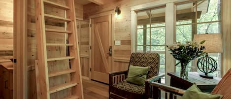 A wooden interior with a chair, a table, and a window with a view of trees.