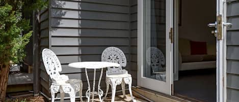 A patio with two white chairs and a table, a sliding glass door, and a small tree.