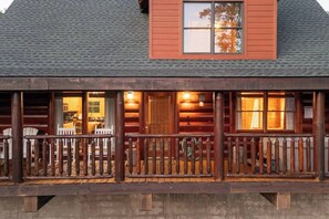 A log cabin with a porch, wooden railings, and a visible interior with a dining area. - Mtn Views! Hot tub! 2 Pools! Mini Golf! Family fun (Sevierville)