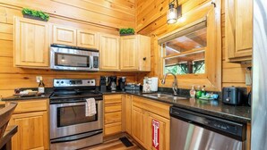 Une cuisine rustique dans un chalet en bois, équipée d’appareils électroménagers en acier inoxydable, d’une machine à café et d’un extincteur.