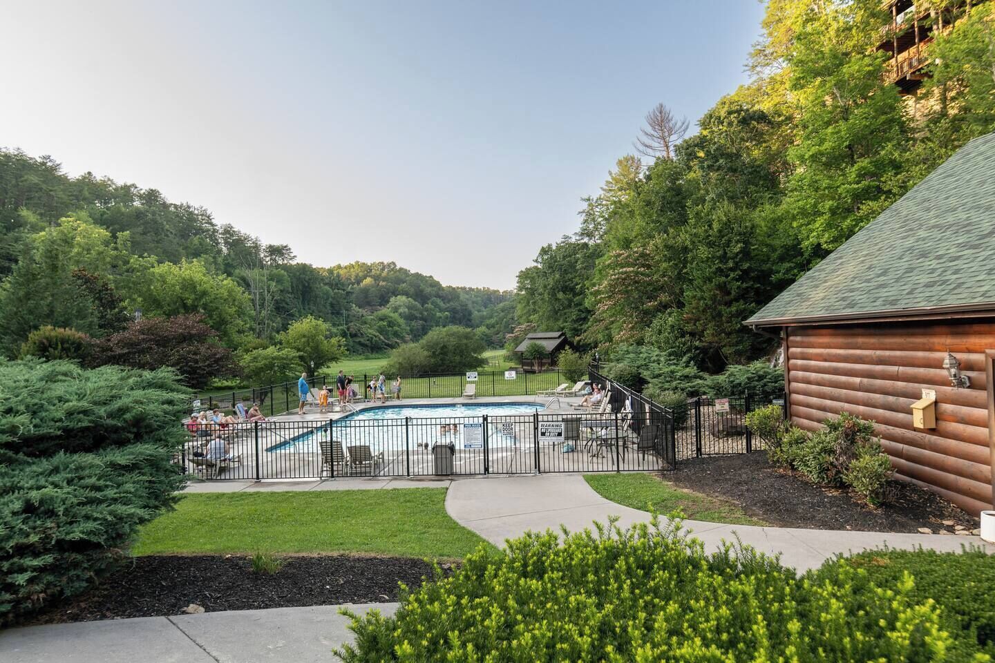 A swimming pool with a wooden cabin and a fenced area, surrounded by lush greenery.