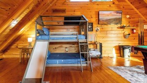 Une chambre mansardée chaleureuse avec des lits superposés, une échelle, un petit bureau, une télévision et une table de billard.