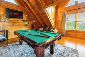 Ein Billardtisch in einem Raum mit Holzwänden, einem Fernseher mit der Aufschrift 'NETFLIX' und einem Schild mit der Bezeichnung 'GATE ROOM'.
