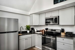 A modern kitchen with stainless steel appliances, white cabinetry, and a granite countertop. - Updated Chalet-Cabin with Hot Tub, Fire Pit, Resort Amenities Surrounded by Amazing Views - the Perfect Getaway for Your Group in Hedgesville, WV (Hedgesville)