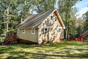 Une petite cabane en bois avec un toit en pente, une terrasse avec des escaliers et une chaise rouge à l’extérieur.