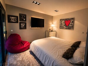 Ein Schlafzimmer mit einem Bett, einem roten Sitzsack, einem Fernseher und Wandbildern.