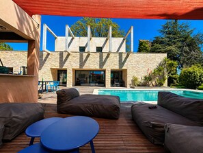 Ein Poolbereich mit Holzterrasse, Sitzgelegenheiten im Freien und einem Steinhaus im Hintergrund.