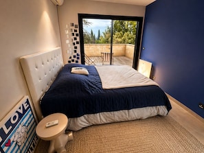 Ein Schlafzimmer mit Bett, kleinem Tisch, Wanddekoration und Blick ins Freie.