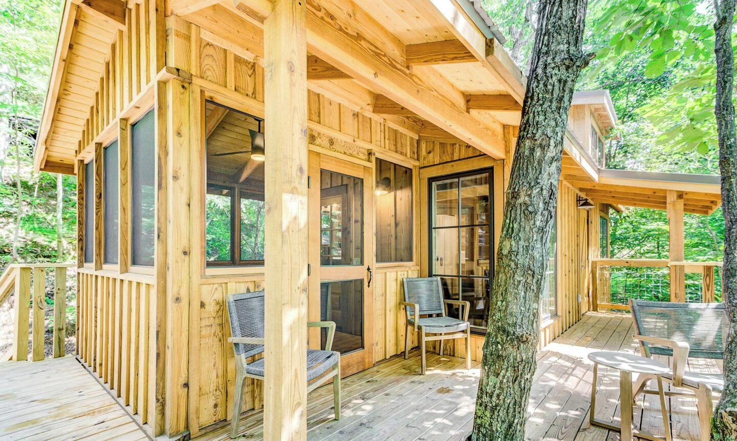 Una cabaña de madera con terraza, ventanas amplias y mobiliario exterior.