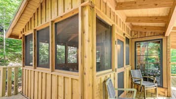 A wooden cabin with large windows, a deck, and outdoor seating.