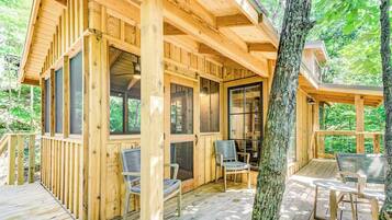 Une cabane en bois dotée d’une terrasse, de grandes fenêtres et de meubles pour s’asseoir à l’extérieur.
