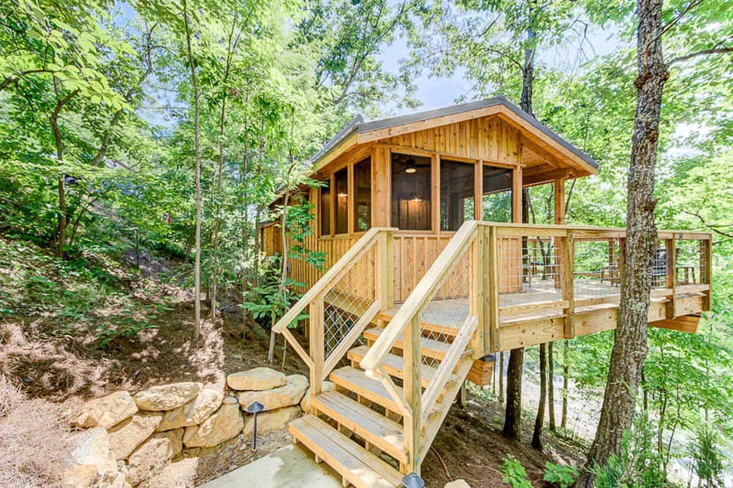 A wooden cabin with a staircase leading to a deck, surrounded by trees.