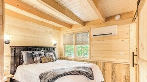 A wooden cabin bedroom with a bed, window, and air conditioning unit. - Secluded Tree House with Barbecue and Hot-tub in Gatlinburg, Tennessee (Gatlinburg)